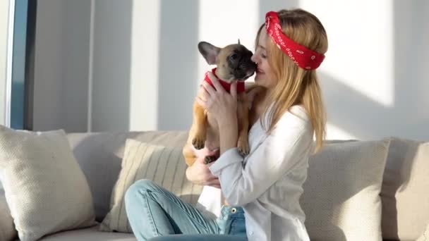 Mujer joven en una camisa blanca y jeans se sienta en el sofá y juega con su perro — Vídeo de stock