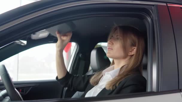 Piękna kobieta spogląda w lustro w samochodzie w salonie samochodowym — Wideo stockowe