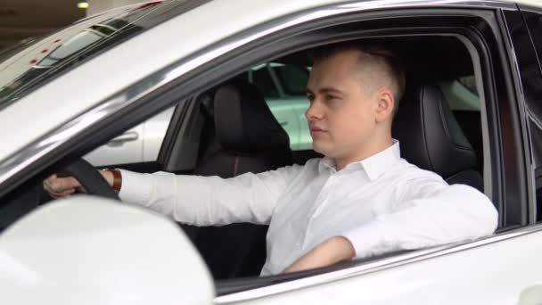 Πορτρέτο ενός νεαρού άνδρα με αυτοπεποίθηση κάθεται σε ένα νέο αυτοκίνητο σε μια αντιπροσωπεία αυτοκινήτων — Αρχείο Βίντεο