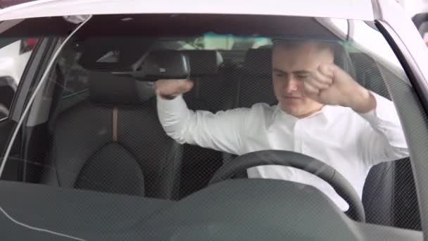 Wesoły człowiek raduje się z kupna nowego samochodu w salonie samochodowym. Mężczyzna uśmiecha się i tańczy w nowym samochodzie w salonie samochodowym — Wideo stockowe
