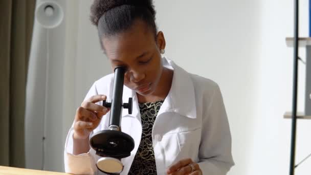 Африканская женщина-ученый делает некоторые исследования и смотрит через микроскоп в лаборатории — стоковое видео