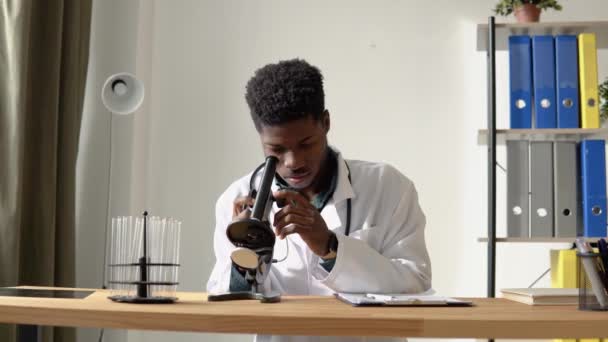 Jeune scientifique afro-américain regardant à travers un microscope dans un laboratoire — Video