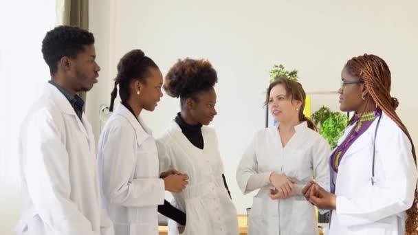 Los estudiantes de medicina, incluidos hombres y mujeres internacionales, tienen una conversación de negocios mientras están en una clínica. Estudiantes de medicina pasantes en la universidad — Vídeo de stock