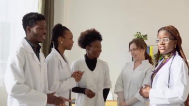 Aralarında uluslararası erkek ve kadınların da bulunduğu bir grup doktor, klinikte dururken iş görüşmesi yapıyor. Tıp öğrencileri üniversitede stajyerler.