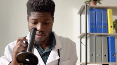 Afrikalı erkek doktor patojen örnekleriyle çalışıyor. Genç Afrikalı Amerikalı bilim adamı bir laboratuarda mikroskoptan bakıyor.