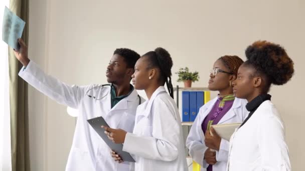 The surgeon and the nurses is monitoring x-ray of a patient. A group of four african american doctors discuss an x-ray — Stock Video