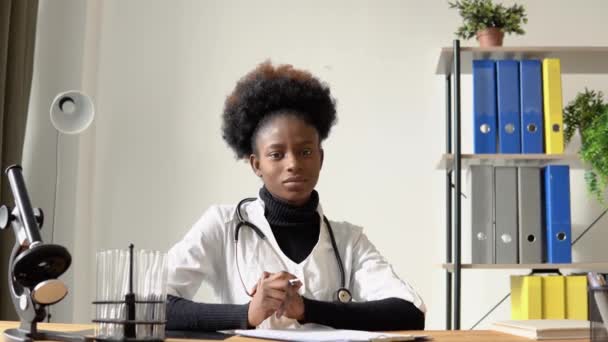 Médecin afro-américaine regardant la caméra alors qu'elle était assise à table à l'hôpital — Video