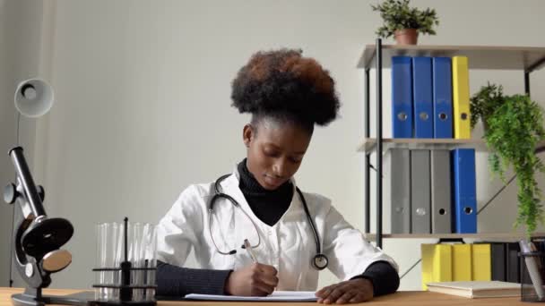 非洲裔美国女医生坐在医院餐桌前，写下病人病史 — 图库视频影像