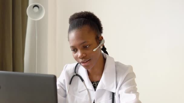 Junge afrikanisch-amerikanische Ärztin mit Headset beim Chatten oder Konsultieren auf dem Laptop. Ärztin trägt Kopfhörer und hält medizinische Online-Konferenz ab — Stockvideo