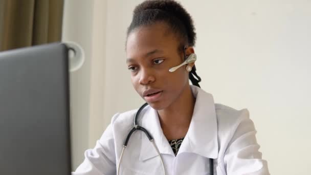 Junge afrikanisch-amerikanische Ärztin mit Headset bei Chat oder Konsultation am Laptop — Stockvideo