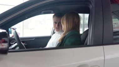 Şık bir adam araba kuaföründe oturup kadın araba satıcısıyla konuşuyor. Profesyonel yardım istemcisi galerideki en iyi otomobili seçiyor