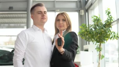 Yeni arabasının anahtarlarını galeride gösteren mutlu bir çift. Otomobil işi, araba satışı.