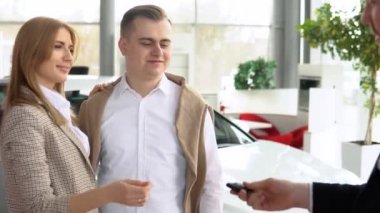 Erkek satıcı mutlu çiftin anahtarlarını veriyor ve memnun müşterinin elini sıkıyor. Otomobil işi, araba satışı, teknoloji ve insan konsepti