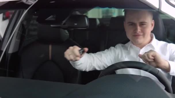 Vrolijke man verheugt zich in het kopen van een nieuwe auto. Een man lacht en danst in een nieuwe auto bij een autodealer — Stockvideo