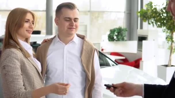 Férfi kereskedő adja át a kocsikulcsot boldog párnak és kezet ráznak elégedett ügyfeleikkel. Autó üzlet, autó eladás, technológia és az emberek koncepció — Stock videók