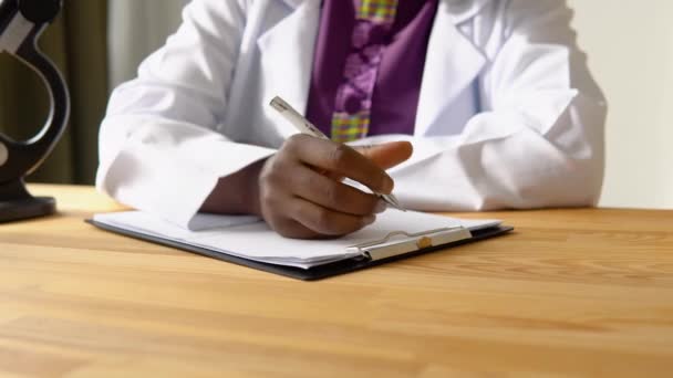 Close-up de mãos de Africano americano médico feminino escrevendo história médica do paciente enquanto sentado à mesa no hospital — Vídeo de Stock