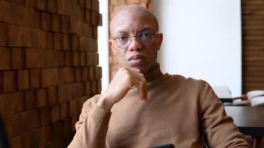 Deve kaşmir kazaklı Afrikalı genç bir adam. Şık, yakışıklı iş adamı. Bir kafede çalışma gününün estetiği. Serbest, uzaktan kumandalı. Videoportrait