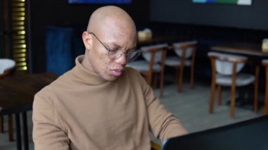 Yüzünde çiller olan Afrikalı Amerikalı bir adam dizüstü bilgisayarda klavyeyle mesaj atıyor. Ellerin yakın görüntüsü