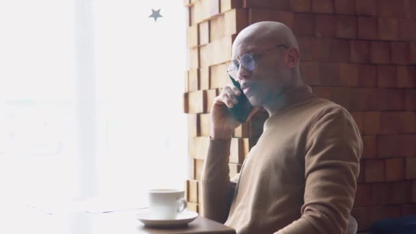 Yüzünde çiller olan Afrikalı Amerikalı genç bir iş adamı pencerenin kenarında bir telefon bekliyor.. — Stok video