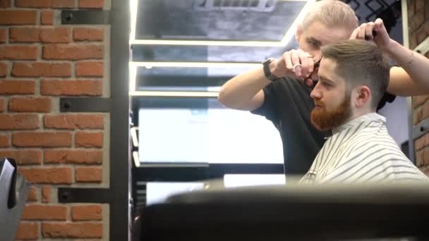 一个留着胡子的年轻人正在理发时坐在理发师的椅子上。侧视图 — 图库视频影像