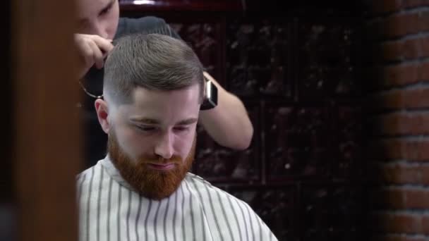 El proceso de corte de pelo para hombre en una elegante barbería con un interior brutal negro y terracota — Vídeo de stock