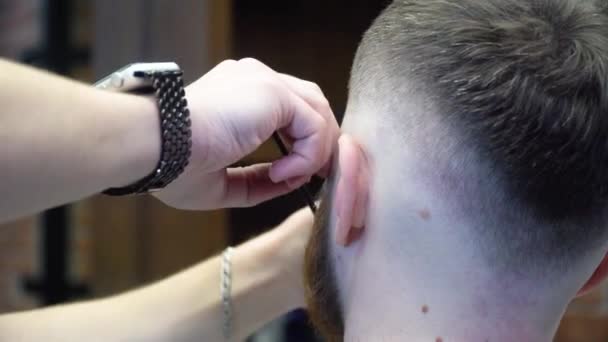 O processo de cortar uma barba vermelha com uma navalha perigosa em uma barbearia — Vídeo de Stock