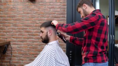 Berber, müşterinin kafasının arkasında saç kesme makinesi kesiyor. Yan görünüm