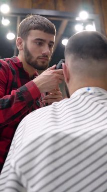 Genç berber müşteriyi çok dikkatli bir şekilde budayıcı ile keser. Dikey video