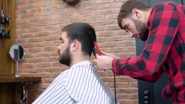 Joven peluquero elegante corta el pelo de los clientes en una barbería — Vídeo de stock