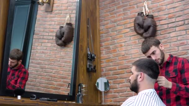 Jeune coiffeur et client lors d'une coupe de cheveux dans un salon de beauté de chaussures. Vue miroir — Video