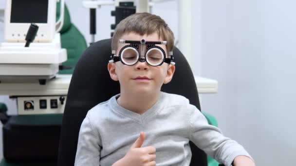 Malý chlapec ve zkušebním rámu pro výběr čoček sedí v obchodě s optikou — Stock video