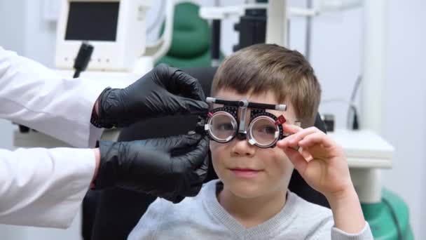 L'ophtalmologiste sélectionne des lentilles pour le garçon au moyen d'une monture d'essai pour la sélection des lentilles — Video