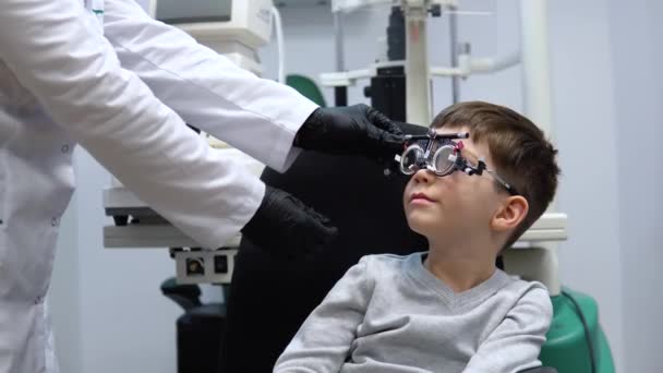 El oftalmólogo hace ajustes en el marco del ensayo para seleccionar lentes para el niño — Vídeo de stock