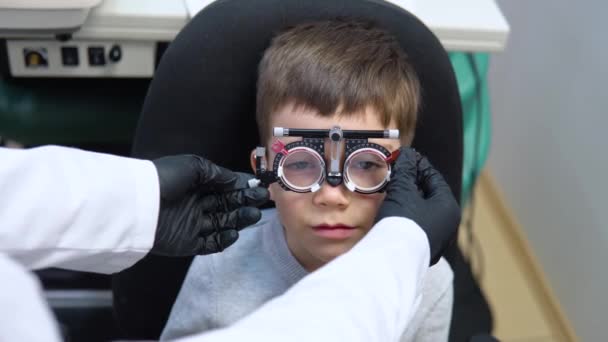 Un niño se sienta en una silla en una cita con un oftalmólogo para recoger lentes de contacto — Vídeos de Stock