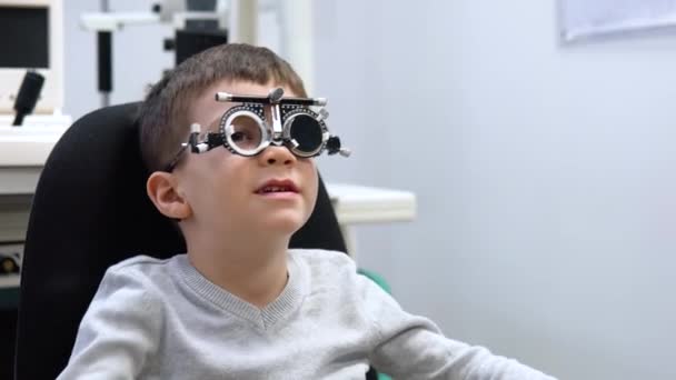 El niño se sienta en una silla en una cita con un oftalmólogo y sigue las instrucciones de los médicos — Vídeos de Stock