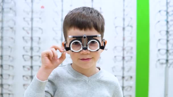 Der Junge steht auf dem Hintergrund eines Schaufensters mit Brillengestell mit Vorrichtung zur Auswahl von Kontaktlinsen — Stockvideo