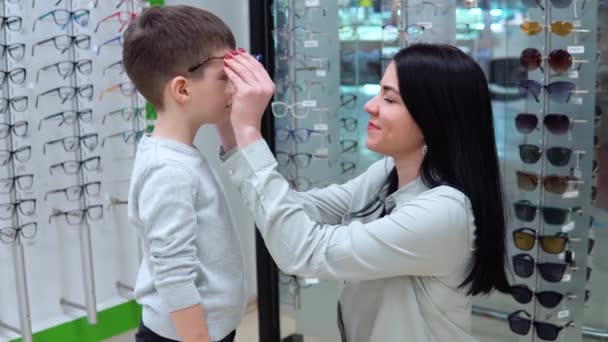 Νεαρή λευκή γυναίκα με μωρό, μητέρα και γιο που διαλέγει γυαλιά σε κατάστημα οπτικών — Αρχείο Βίντεο