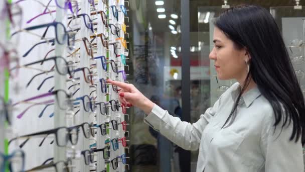 Νεαρή καυκάσια γυναίκα διαλέγει γυαλιά σε κατάστημα οπτικών — Αρχείο Βίντεο