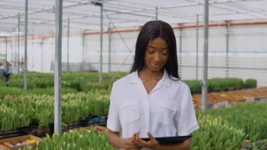 Genç bayan çiçekçi, lalelerle serada duran bir tablette çalışıyor.