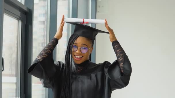 A joyful graduate holds a diploma over her head and poses for the camera. African american woman with higher education — Wideo stockowe