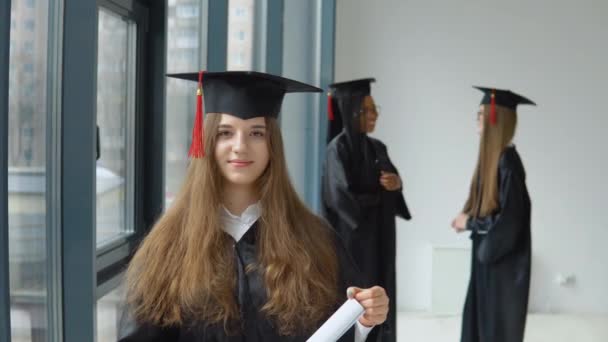 Um graduado sorrindo detém um diploma de ensino superior em suas mãos com outras estudantes do sexo feminino em formação. Programa internacional de intercâmbio de estudantes para grupos socialmente vulneráveis — Vídeo de Stock
