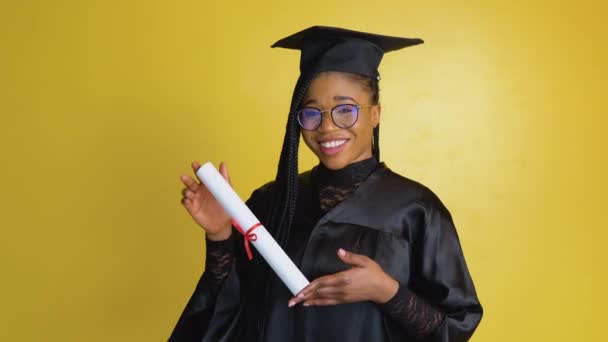 Mujer afroamericana tiene maestría después de graduarse de la universidad. Feliz estudiante femenina con diploma en fondo amarillo — Vídeo de stock