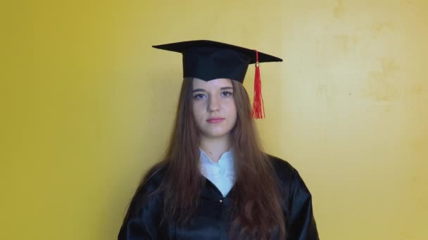 Biała studentka poprawia kapelusz na głowie, stojąc przed kamerą z dyplomem ukończenia szkoły. Tytuł magistra edukacji — Wideo stockowe