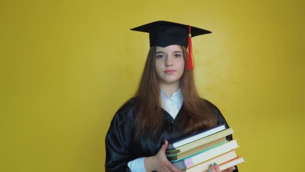 Jovem estudante caucasiano mantém muitos livros enquanto permanece na frente da câmera no fundo amarelo — Vídeo de Stock