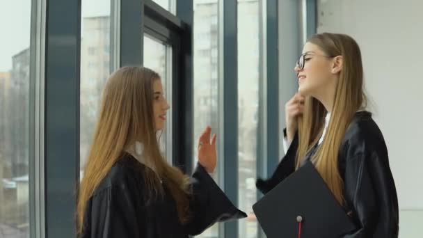 Двоє молодих щасливих випускників щасливо спілкуються біля вікна — стокове відео