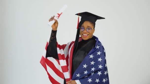 Happy Stylish Afro American Woman Student In Graduate Uniform Shows Diploma segurando bandeira dos EUA nos ombros. Educação dos EUA — Vídeo de Stock