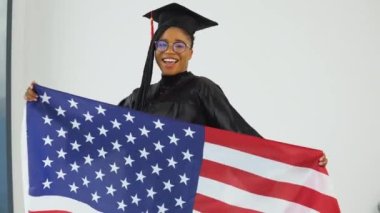 Önünde Amerikan bayrağı taşıyan, üniformalı mutlu Afro-Amerikan bayan öğrenci. Ortalama plan