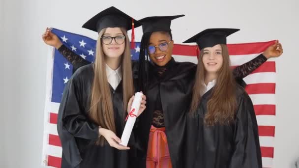 ABD Üniversitesi 'nin üç bayan öğrencisi mezuniyet kıyafeti ve şapka giyiyor. Bir tanesinin yüksek lisans diploması var. — Stok video