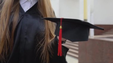 Üniversite mezunu birinin elinde kırmızı püsküllü usta şapkası. Dış arkaplan ile görüntüyü kapat