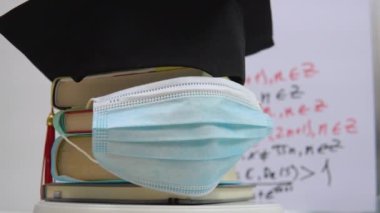 Bir salgın sırasında üniversite eğitiminin tamamlanması. Kitaplar, mezuniyet şapkası ve koruyucu tıbbi maske. Eğitim kavramı